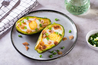 Egg baked in avocado sprinkled with bacon and herbs on a plate