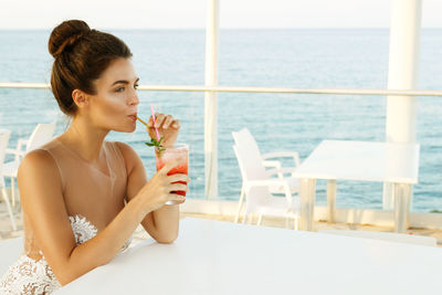 Beautiful woman drinking cocktail at restaurant against sea