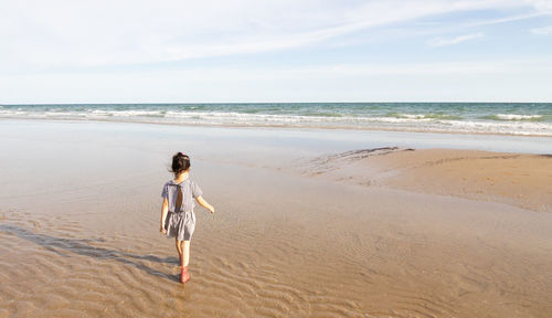 Shot of little asian black hair kid girl with copy space is walking on wavy sand beach alone 