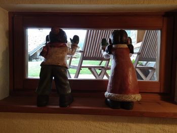 Rear view of friends standing against window at home