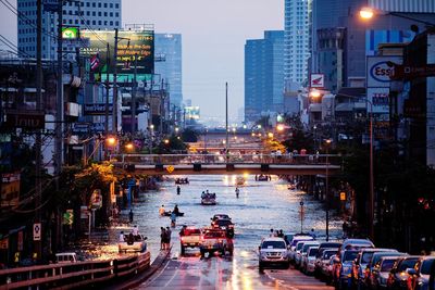 People and vehicles on road during floods in city at dusk