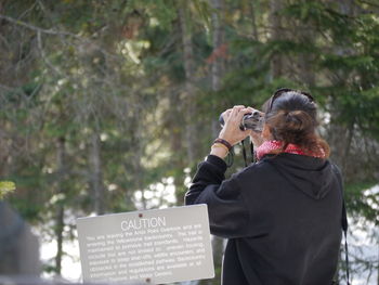 Young woman holding camera while standing on white wall