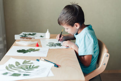 8 years old child sitting by desk and doing herbarium on album sheet. autumn activities for children