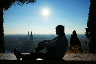Silhouette of woman sitting on retaining wall against sky