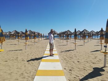 Full length of man standing on boardwalk at beach against blue sky