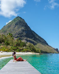 Rear view of woman sitting on beach against sky