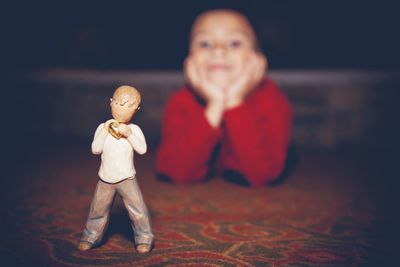 Close-up of figurine against boy with hand on chin lying on floor at home