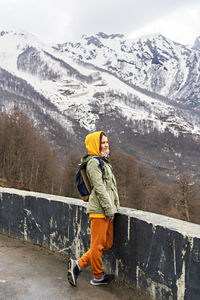 Young woman in yellow hood side view against the background of caucasian mountain snow covered peaks 