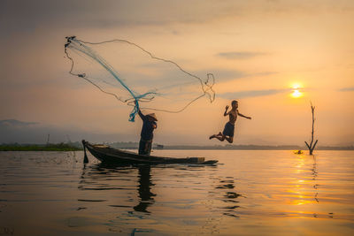 Boy jumping by fisherman throwing net in river during sunset 