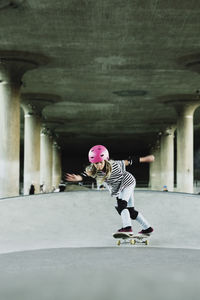 Full length of confident girl skateboarding against columns at park