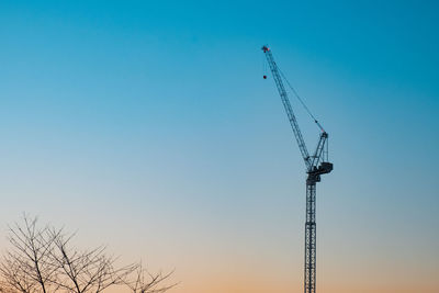 Low angle view of silhouette crane against clear blue sky