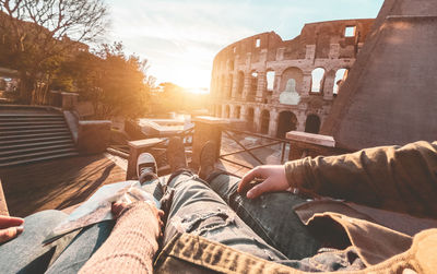 Low section of man sitting against built structure