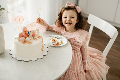 A laughing little girl eats a birthday cake on her birthday at home