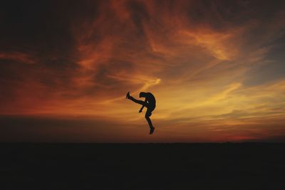 Silhouette man jumping against orange sky