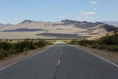 Road leading towards mountains against sky