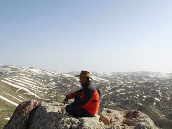 Man sitting on mountain against clear sky