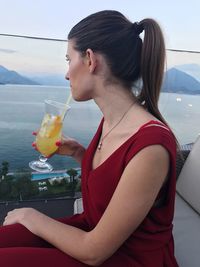 Young woman looking at sea while drinking juice during sunset