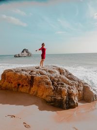 Man standing on rock at beach against sky