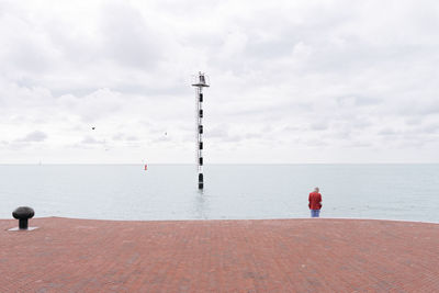 Rear view of person standing next sea against cloudy sky