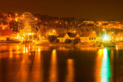 Illuminated cityscape by river against sky at night