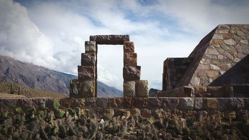 Cactus growing by old ruins against sky