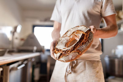 Midsection of baker holding round bread in bakery 