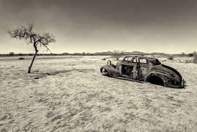 Abandoned car on landscape against sky