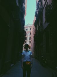 Rear view of man walking on street amidst buildings