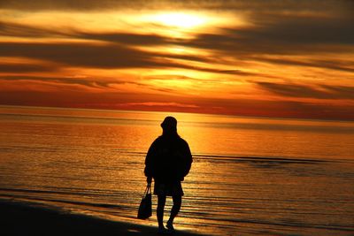 Silhouette mature woman standing at beach against sky during sunset