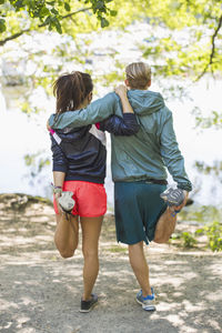Full length rear view of couple doing stretching exercises together at lakeshore
