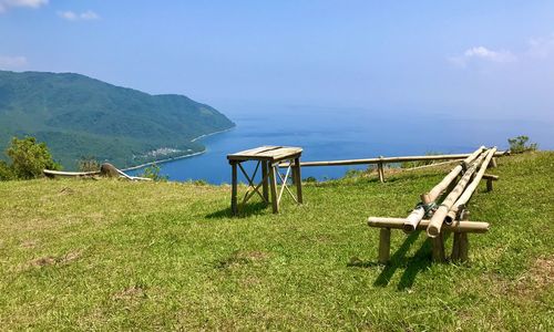 Deck chairs on field by sea against sky