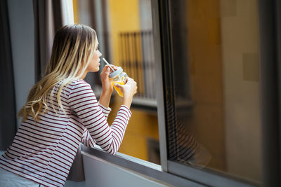 Side view of woman drinking glass at home