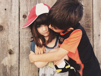 Cute sibling embracing against wooden wall