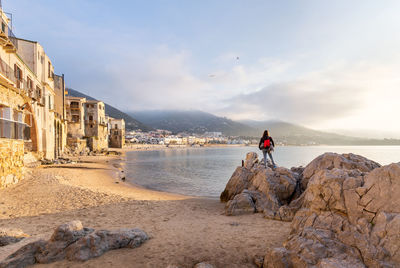 Man on rock at beach against sky