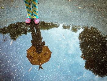 Girl standing with umbrella reflecting on puddle during rainy season