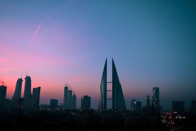 Illuminated buildings in city against sky during sunset