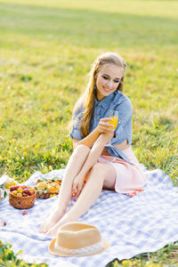 Beautiful young woman in a blue denim shirt and pink skirt in the garden at a picnic holding a glass