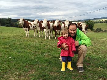 Portrait of happy father and daughter by cows on grassy field