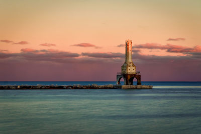 Silhouette lighthouse by sea against sky during sunset