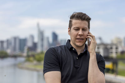 Close-up of young man talking on mobile phone with city in background
