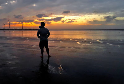 Rear view of man on beach against sky during sunset