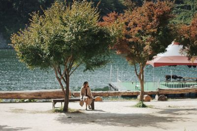 Young woman sitting on riverbank against trees