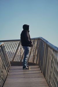 Rear view of man walking on footbridge against clear sky