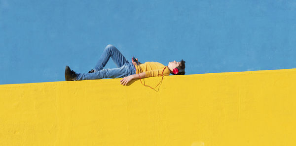 Side view of man lying on yellow wall