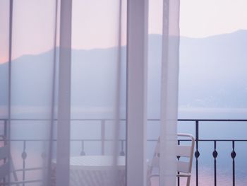 Table and chairs against sky seen through glass window