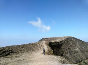 Rear view of man walking on rock formation against sky