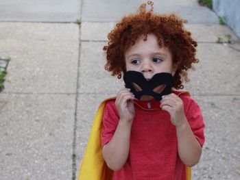 Boy with curly redhead wearing costume standing on footpath