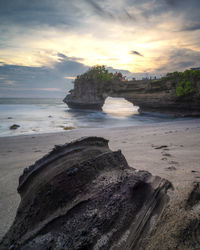 Rock formation on beach against sky during sunset