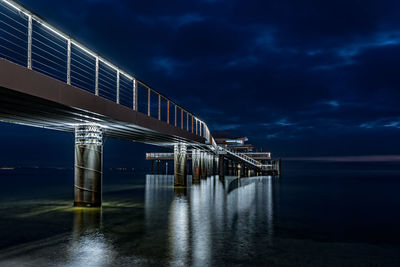 Illuminated bridge over sea against sky at night