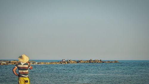 Rear view of woman by sea against clear sky